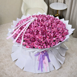 An exceptionally large, oversized bouquet of 500 fresh pink and purple roses wrapped in sculptural white designer paper with long purple and pink branded ribbons.