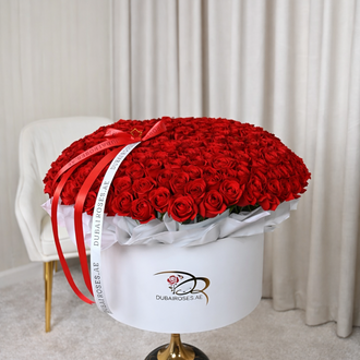 A massive, oversized white circular designer box filled with 200 fresh red roses, featuring long-trailing red and white branded ribbons.