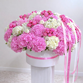 A massive, over-the-top luxury flower box filled with vibrant pink hydrangeas, white hydrangeas, and pink garden roses on a white pedestal.