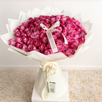 A close-up of a premium large-scale bouquet featuring 100 dense, fresh deep purple roses in a professional designer white wrap.