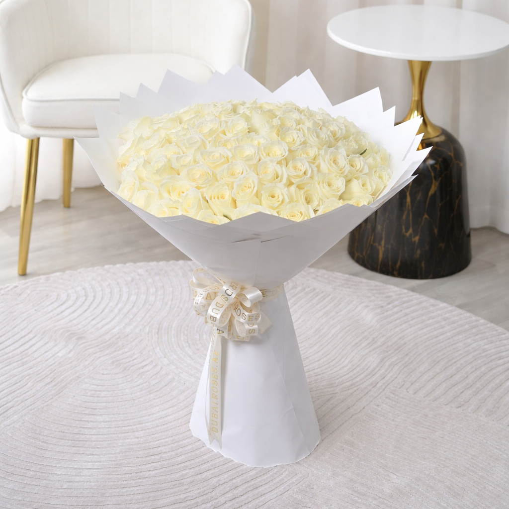 100 white roses bouquet on a white pedestal table in a room with a white chair and black side table.