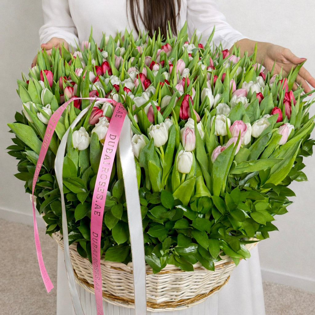 Woman holding a large basket of tulips with pink ribbons against a plain background