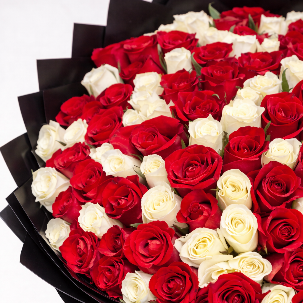 A massive, grand-scale bouquet featuring 100 fresh red and white roses expertly arranged and wrapped in premium black pleated paper with long-trailing red ribbons.