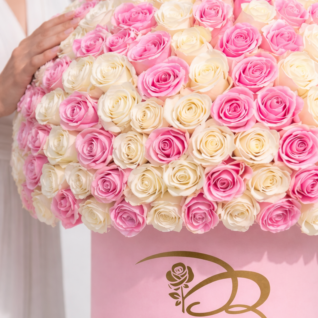 A closeup photo of Pink and white roses in a pink box with a lady hand on the side