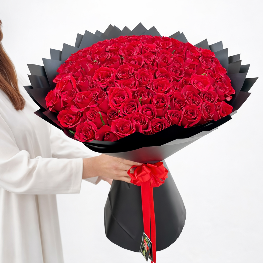 a lady with straight hair and white dress holding a 100 red roses bouquet in black wrapping paper
