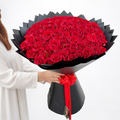 a lady with straight hair and white dress holding a 100 red roses bouquet in black wrapping paper