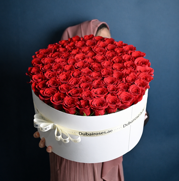 Large bouquet of red roses in a white box with 'DubaiRose' branding against a dark background.
