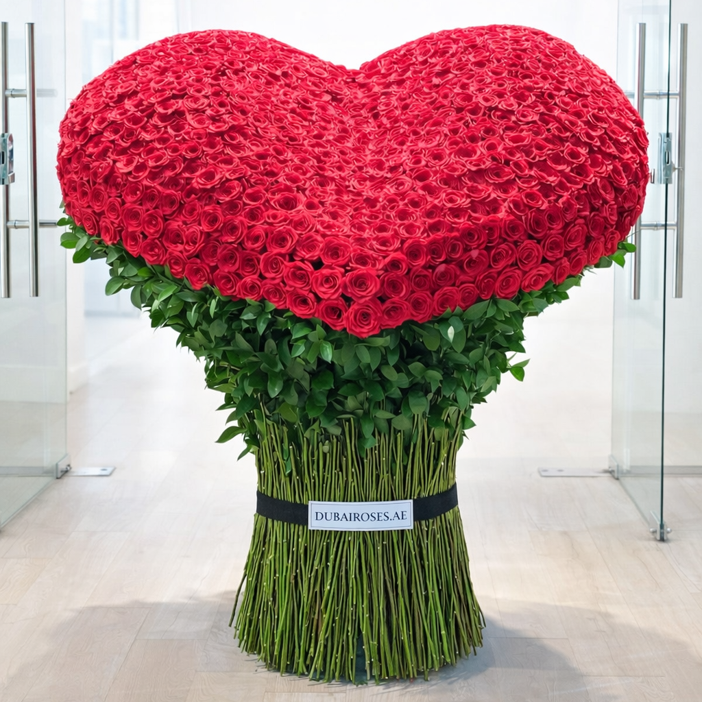 Heart-shaped arrangement of red roses with green leaves on a light wooden floor.