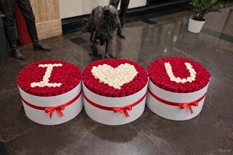 Three large, circular white designer boxes filled with hundreds of red roses, featuring white roses arranged to spell out "I," a heart shape, and "U."