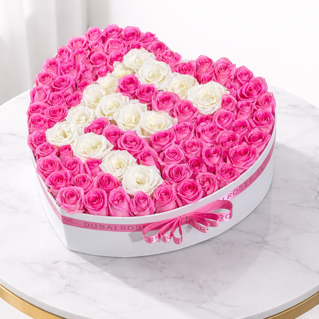 Heart-shaped box of pink and white roses held by a person in a white dress.