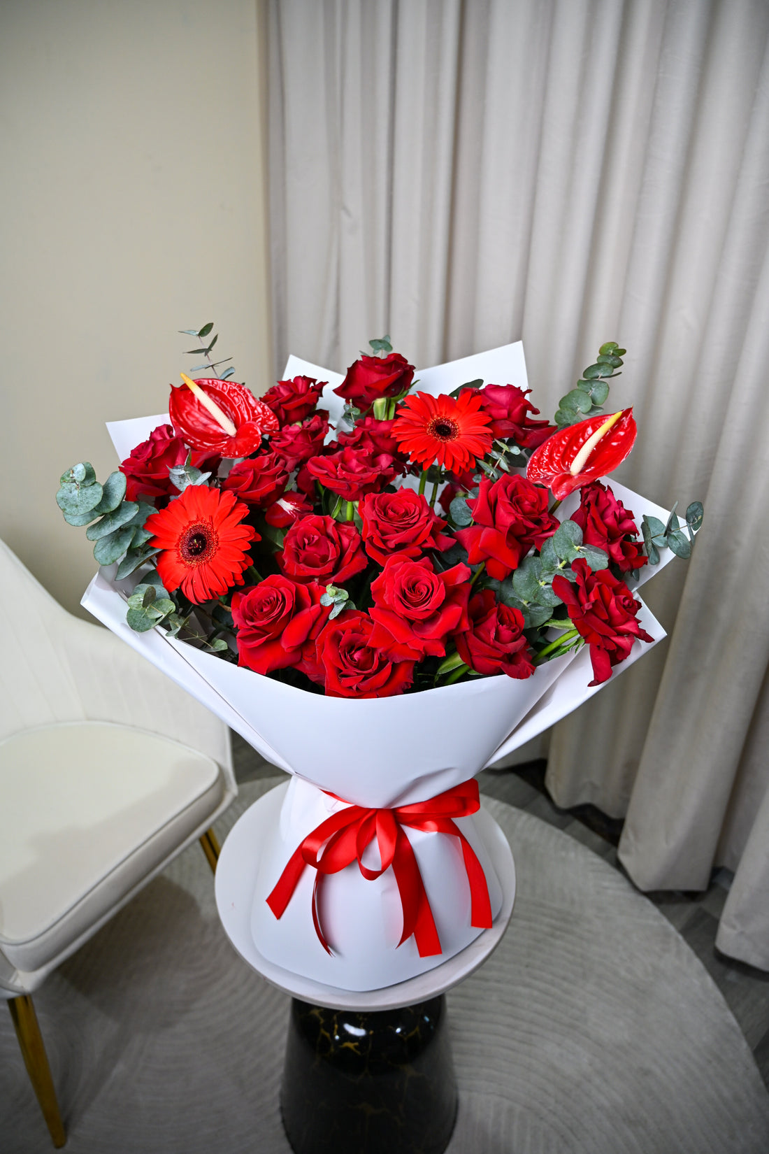 Person holding a bouquet of red composition flowers with a white wrap and red ribbon.