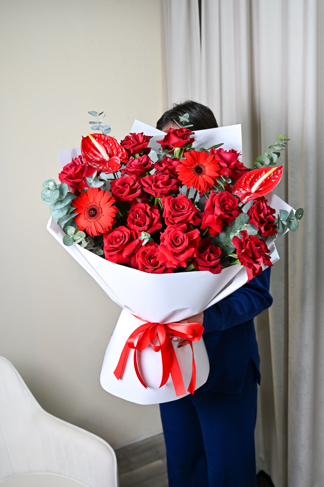 Person holding a bouquet of red composition flowers with a white wrap and red ribbon.