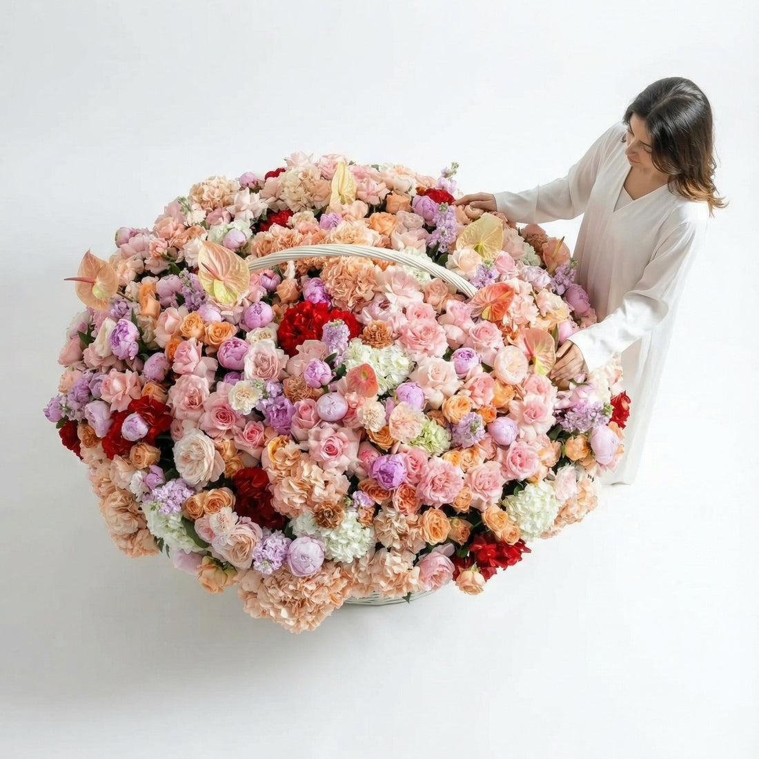 Woman holding a large basket filled with colorful flowers in a bright room.