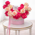 Front view of a round pink gift box overflowing with fresh pink and peach French roses and signature white branded ribbons.