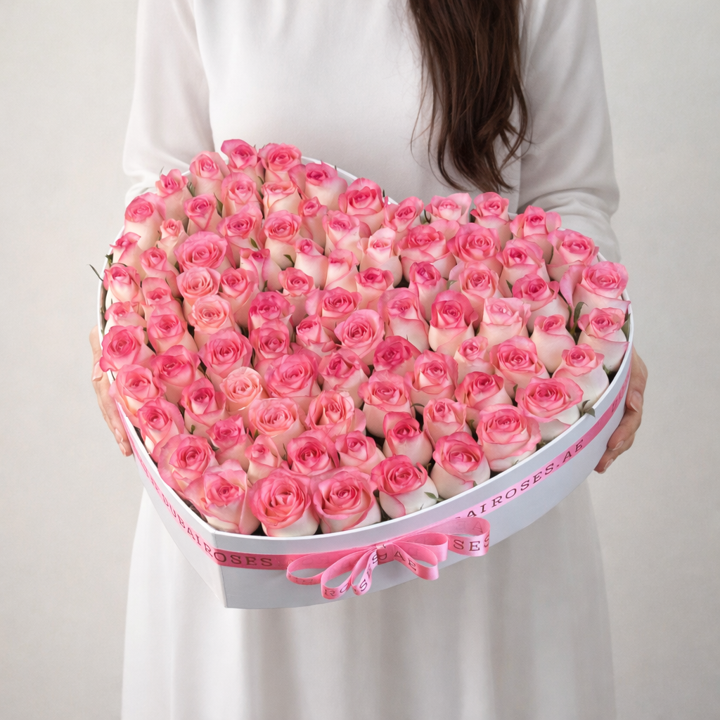 Heart-shaped box of pink roses held by a person against a plain background