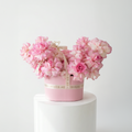 Pink floral arrangement in a decorative box on a white pedestal against a white background