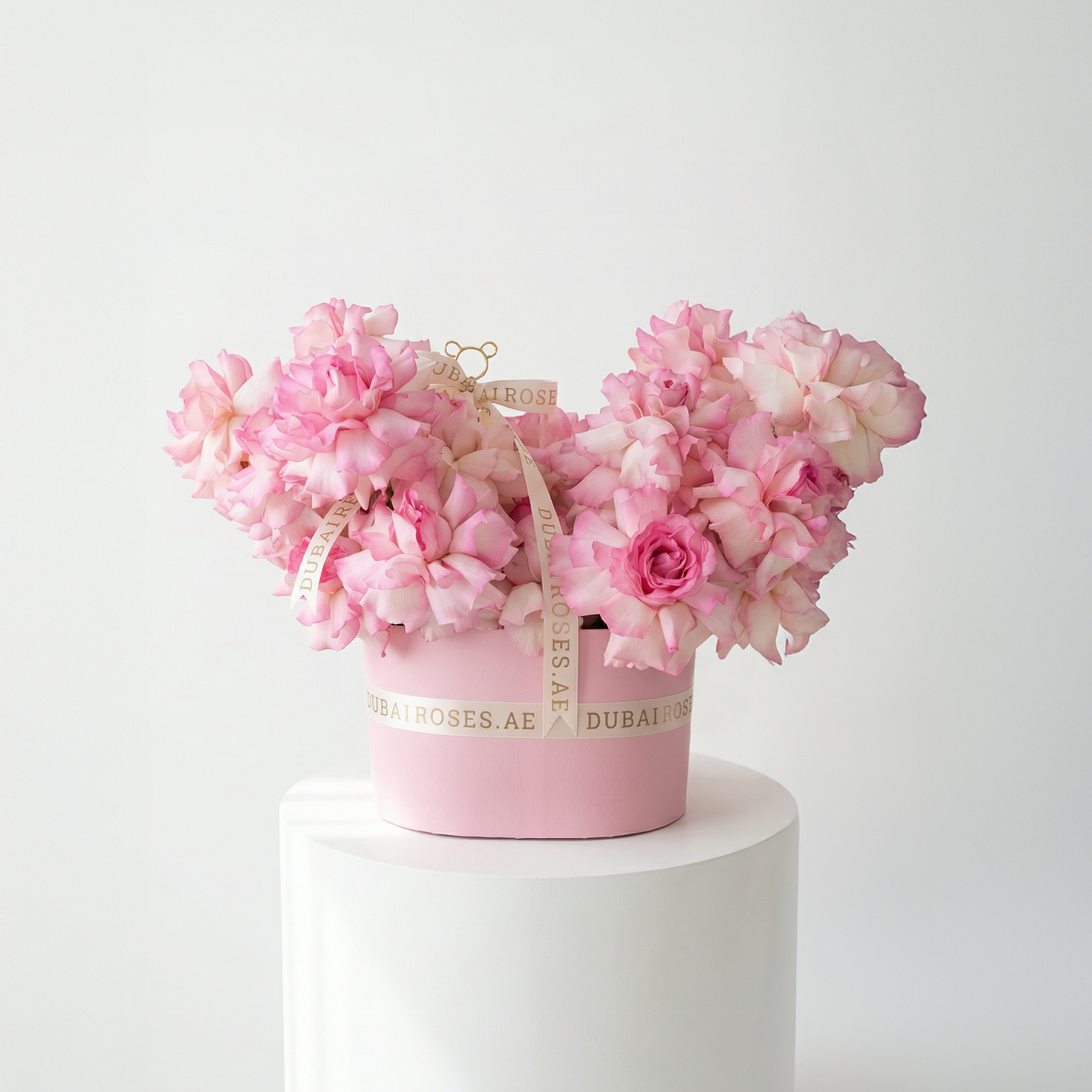 Pink floral arrangement in a decorative box on a white pedestal against a white background