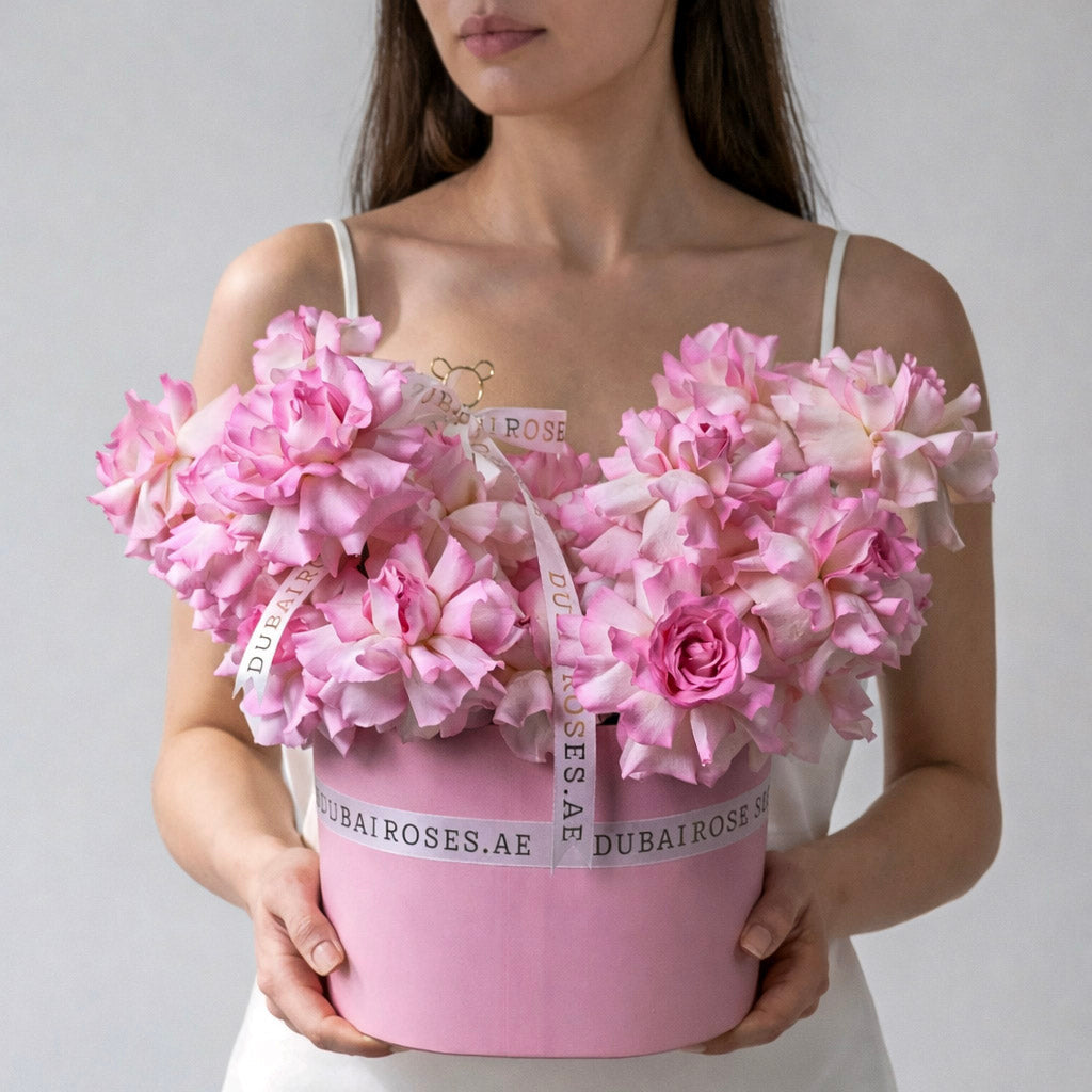 Person holding a pink flower box with pink flowers against a plain background