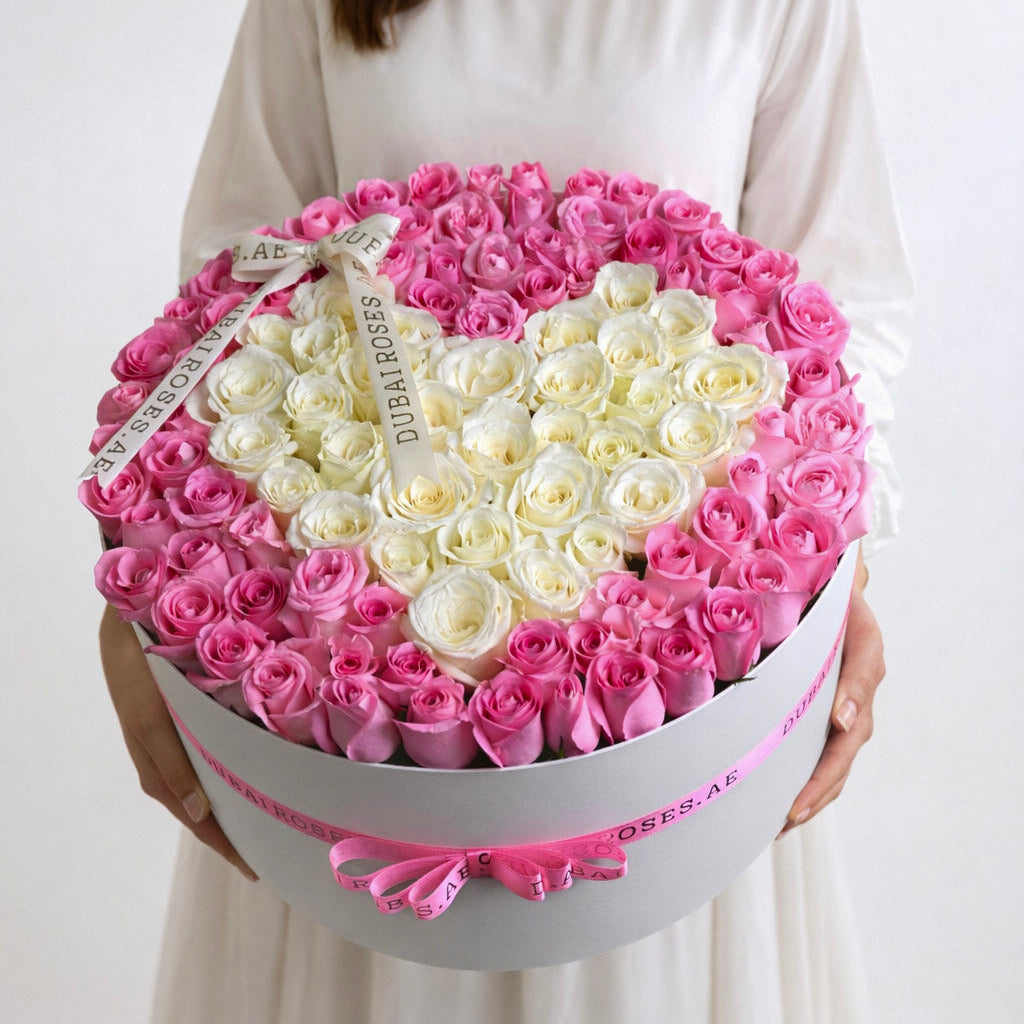 Close-up of a personalized white round luxury rose box with a white heart surrounded by deep pink roses and a decorative pink ribbon.