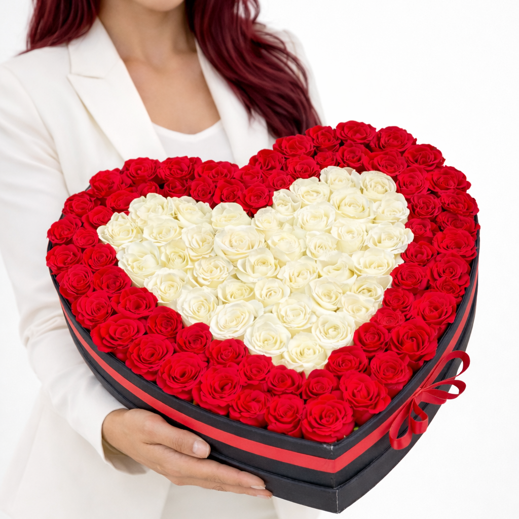 A dense and vibrant arrangement of fresh red roses surrounding a white rose heart in a luxury black heart box.