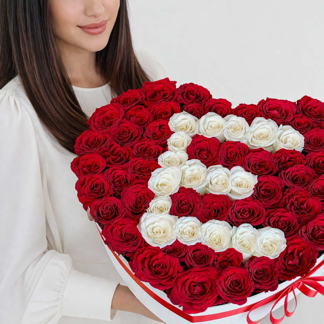 a lady holding a white heart box of red roses with letter E in the middle using white roses against a white background