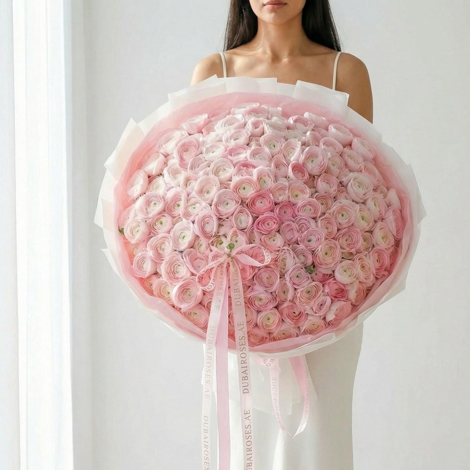 Woman holding a large bouquet of renanculus pink flowers against a white background