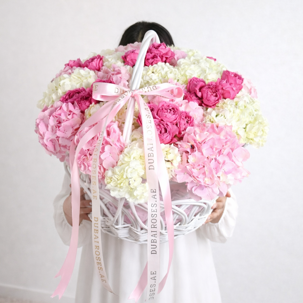 Heart-shaped arrangement of pink and white flowers with a pink ribbon on a textured surface.