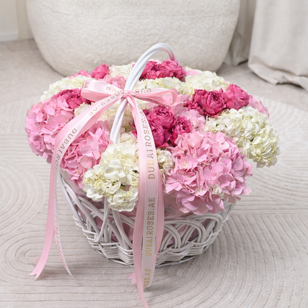 Heart-shaped arrangement of pink and white flowers with a pink ribbon on a textured surface.
