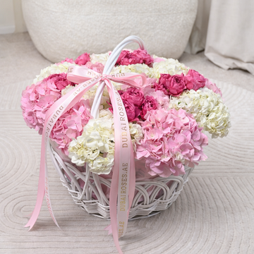 Heart-shaped arrangement of pink and white flowers with a pink ribbon on a textured surface.